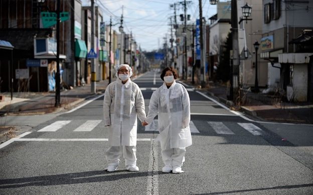 Wearing white protective masks and suits, Yuzo Mihara  and his wife Yuko pose for photographs on a deserted street in the town of Namie, inside the Fukushima nuclear disaster exclusion zone
