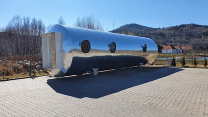 Exterior view of a modern, metallic normobaric oxygen chamber unit placed outdoors on a paved area.