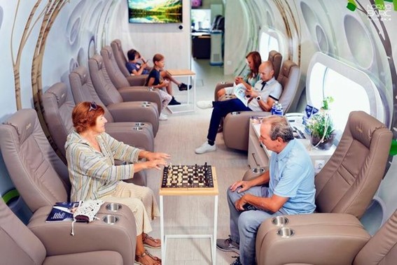 People relaxing in a normobaric oxygen chamber, sitting on reclining chairs, some reading and others playing chess.