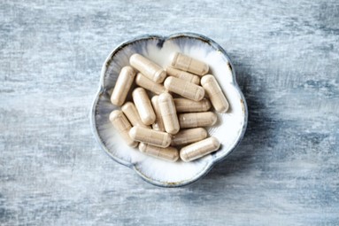 A ceramic bowl filled with beige supplement capsules, placed on a rustic gray surface.