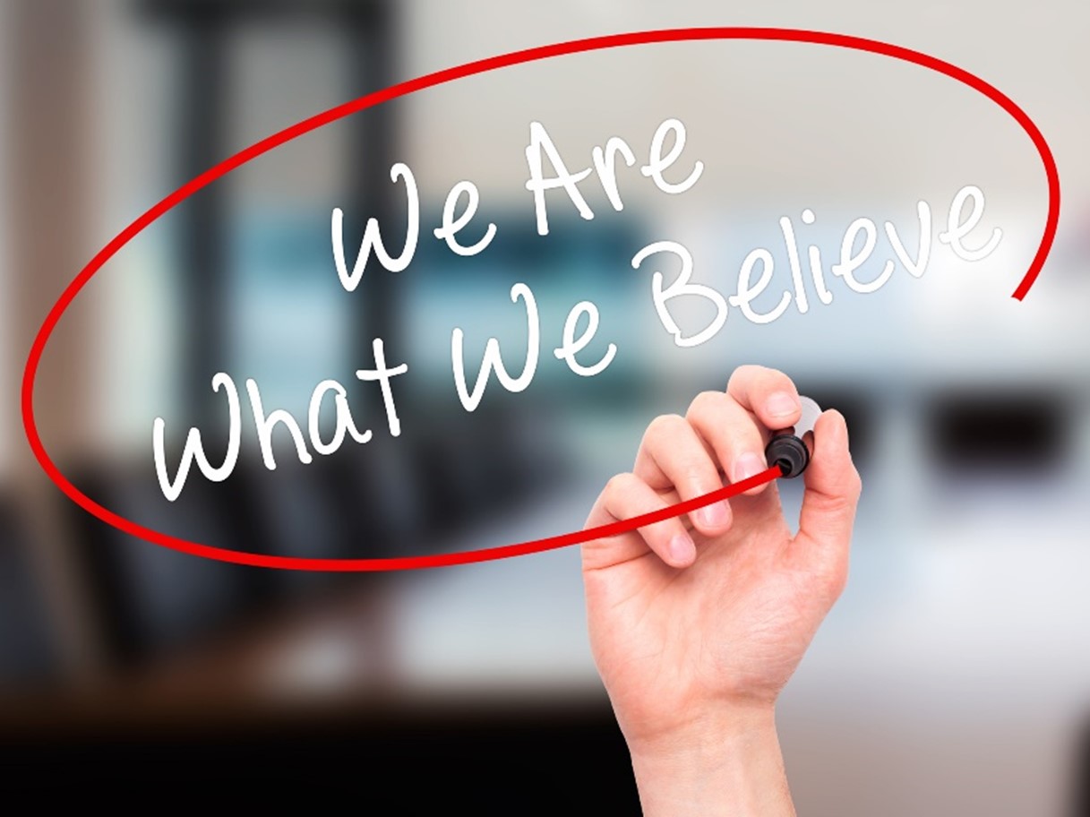 Hand writing the phrase “We Are What We Believe” inside a red circle on a transparent surface, symbolizing the power of belief, mindset, and consciousness shaping reality.
