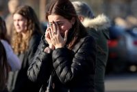 Young woman covering her face in grief outdoors, with others blurred in the background.