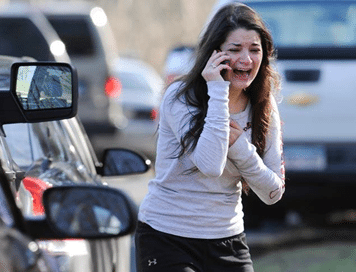 Distressed woman crying while talking on a phone beside parked cars