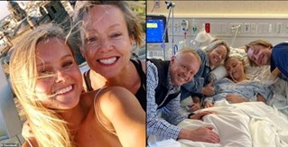 Photo of a smiling young woman standing beside an older man lying in a hospital bed, surrounded by family members.