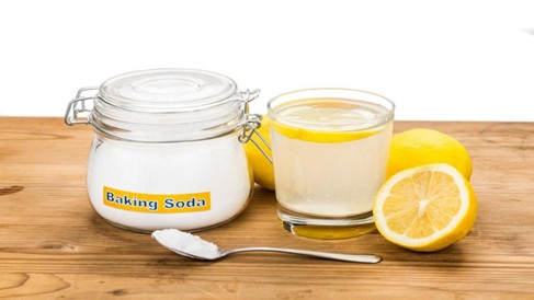 Jar of baking soda beside lemon slices and a glass of lemon water.