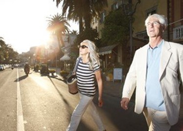 Older couple walking outdoors in bright sunlight.