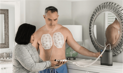 Man using a wearable medical therapy device with adhesive pads on his chest.