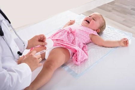 Crying young child lying on an examination table while a healthcare professional prepares an injection.