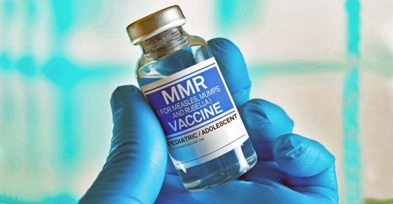 Gloved hand holding an MMR vaccine vial labeled for measles, mumps, and rubella.