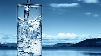 Fresh water being poured into a glass against a natural landscape.